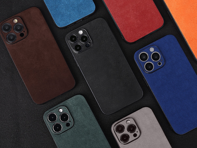 May include: Assortment of ten phone cases in various colours and textures. The cases are made of a soft, suede-like material and feature a raised camera bump. The cases are arranged in a grid pattern on a black background.