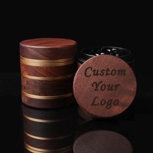 Könnte beinhalten: Ein Kräutermühle aus Holz mit dunkelbraunem Finish und goldenen Bändern. Der Deckel ist mit den Worten "Custom Your Logo" graviert. Die Mühle ist für Kräuter und Gewürze konzipiert.