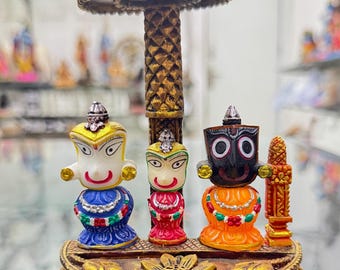 May include: A gold-colored decorative stand with three figures. The figures are painted in bright colors and have detailed facial features. The stand has a round top and a base shaped like a lotus flower.