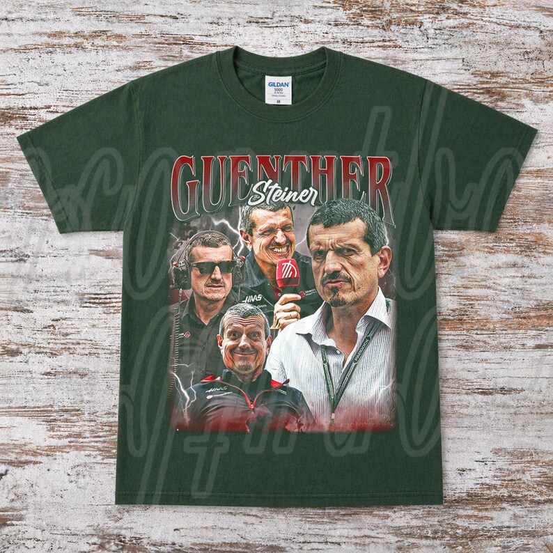 May include: Dark green t-shirt featuring a graphic of G&uuml;nther Steiner, with his name in red and white. The design includes multiple images of Steiner, with a lightning bolt effect in the background. The shirt is a Gildan brand.