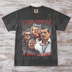 May include: Dark gray t-shirt featuring a collage of images of Guenther Steiner, with the name "Guenther Steiner" in red and white lettering. The shirt has a vintage, distressed look.