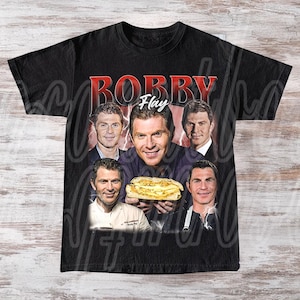 May include: Black t-shirt featuring a graphic of Bobby Flay with multiple images of him, holding a sandwich. The word "Bobby" is in red, with "Flay" in white script. The shirt has a vintage, distressed look.