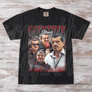 May include: Black t-shirt featuring a graphic of Guenther Steiner, with his name in red and white. The design includes multiple images of Steiner in various poses. The shirt is made of a soft, comfortable material.