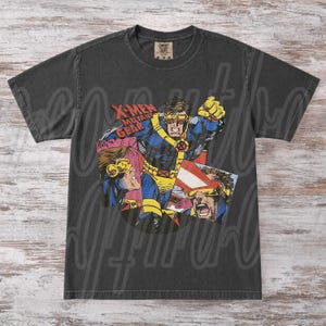 May include: Dark gray t-shirt featuring a comic book illustration of Cyclops from X-Men. The graphic includes the text "X-Men Mutant Gear" and images of Cyclops in action, with yellow and blue accents. The shirt has a vintage, worn look.