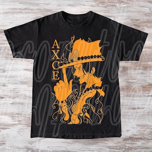 以下が含まれることがあります： 黒いTシャツ。オレンジ色のイラストで帽子をかぶったキャラクターと「ACE」の文字が描かれています。炎と詳細なアートワークが特徴で、大胆なグラフィックを作成しています。