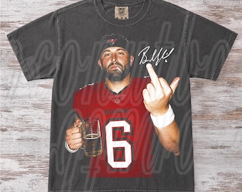 Puede incluir: Una camiseta de manga corta gris carbón con un gráfico de una persona barbuda con una camiseta roja con el número 6, sosteniendo un vaso de cerveza y haciendo un gesto con el dedo medio. La camiseta incluye una firma y el texto PEPPER COLOR.