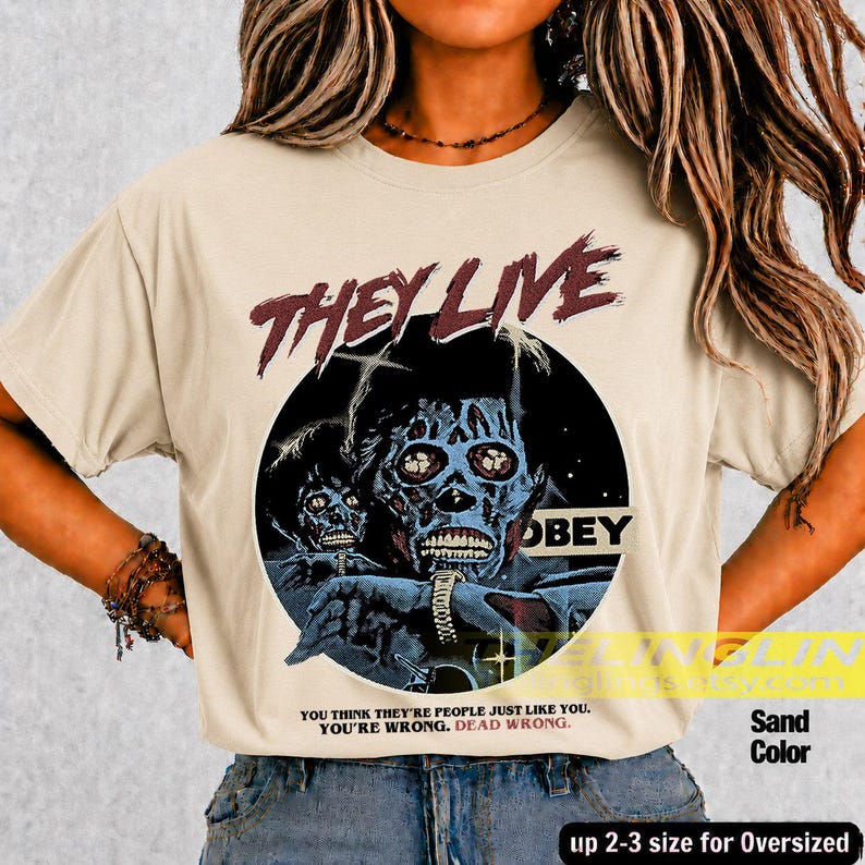 K&ouml;nnte beinhalten: Ein sandfarbenes T-Shirt mit einem Grafikdruck einer skelettartigen Figur und dem Text THEY LIVE sowie OBEY. Unter der Grafik steht der Text: YOU THINK THEY'RE PEOPLE JUST LIKE YOU. YOU'RE WRONG. DEAD WRONG. Das T-Shirt hat einen Rundhalsausschnitt.