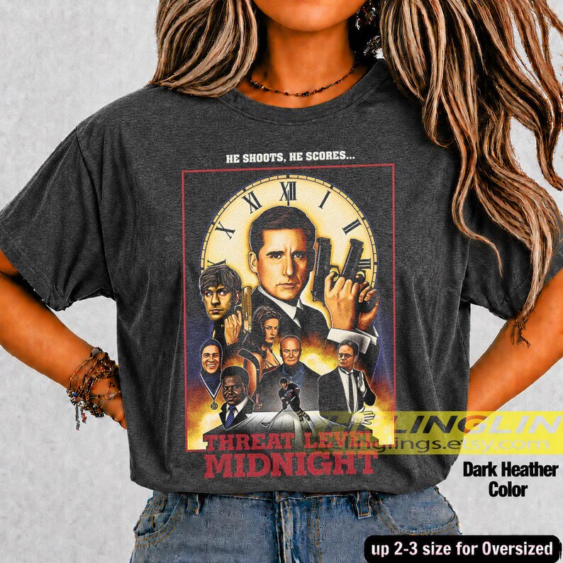 May include: A dark heather gray t-shirt featuring a graphic print with the text HE SHOOTS, HE SCORES... and THREAT LEVEL MIDNIGHT. The design includes a large clock face background and a collage of characters from a television show.