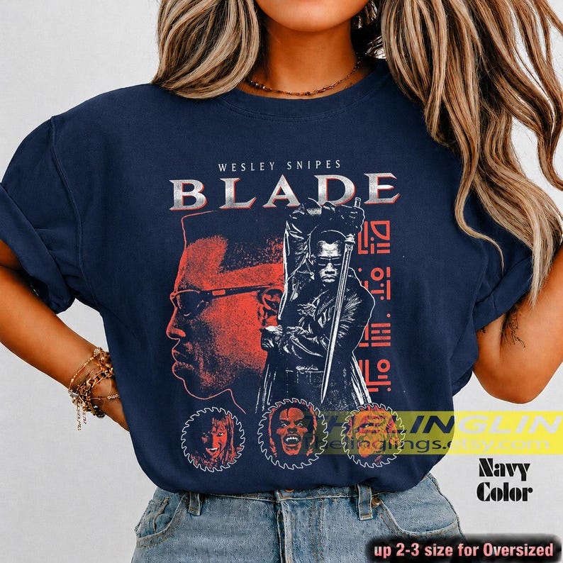 May include: A navy blue t-shirt featuring a graphic print of the film Blade. The design includes the text WESLEY SNIPES BLADE, a large portrait of the character, a figure holding a sword, and three circular character icons at the bottom.