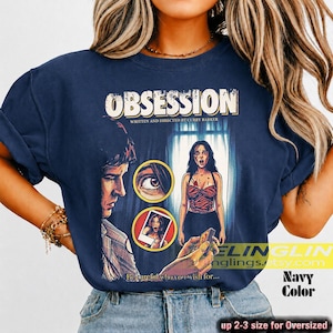 K&ouml;nnte beinhalten: Marineblaues T-Shirt mit dem Wort "OBSESSION" und einem Filmplakat-Grafik. Die Grafik zeigt einen Mann, eine Frau und den Text "WRITTEN AND DIRECTED BY CURRY BARKER." Das Shirt hat auch den Text "Beware who you wish for..." und "Navy Color."