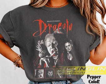 May include: A charcoal gray t-shirt featuring a graphic print of Bram Stoker's Dracula. The design includes a large central image of two characters, with the title in red text above and four smaller square panels showing scenes at the bottom.