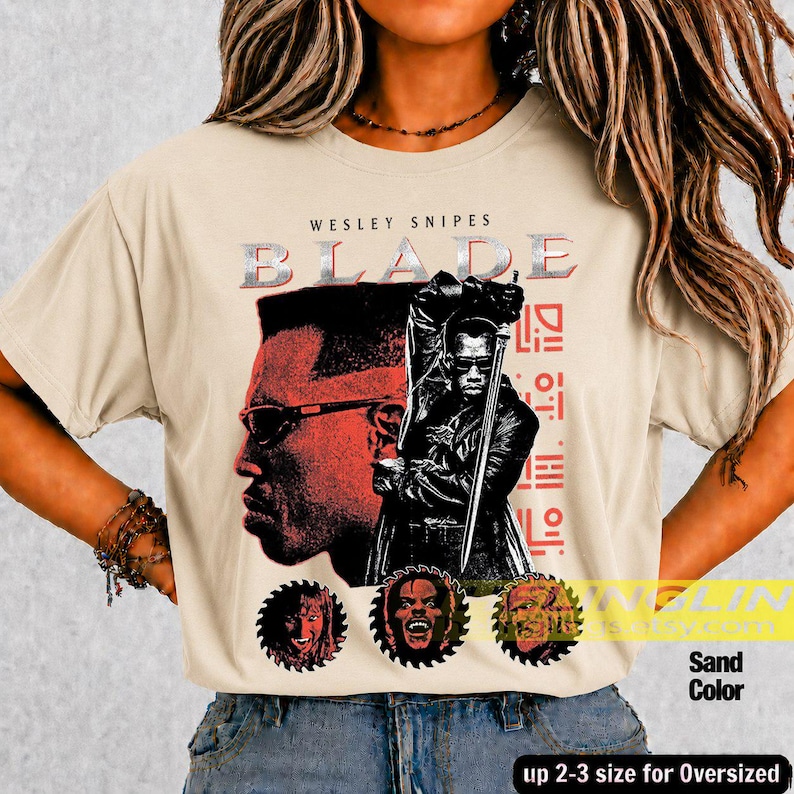 May include: A sand-coloured t-shirt featuring a graphic print of Wesley Snipes as Blade. The design includes a large red-toned profile, a central figure holding a sword, and three circular portraits at the bottom with the text BLADE.