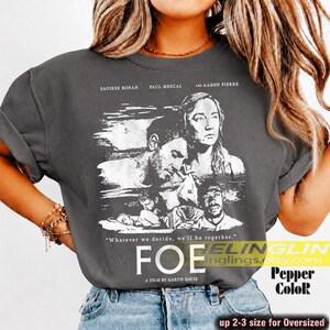 May include: Dark gray t-shirt featuring a black and white graphic from the movie "Foe", with Saoirse Ronan, Paul Mescal, and Aaron Pierre. The text "Whatever we decide, we'll be together" is also visible. The shirt is oversized.