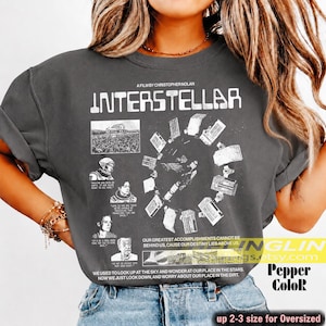 May include: A charcoal gray t-shirt featuring a white graphic print inspired by the film Interstellar. The design includes the movie title, various scene stills, character portraits, and a circular arrangement of spacecraft illustrations with text.