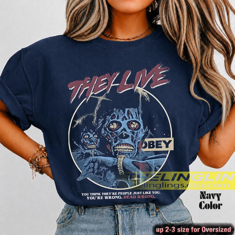 K&ouml;nnte beinhalten: Ein marineblaues T-Shirt mit einem Grafikdruck einer skelettierten Figur und dem Text THEY LIVE sowie OBEY. Unter der Grafik steht der Text: YOU THINK THEY ARE PEOPLE JUST LIKE YOU. YOU ARE WRONG. DEAD WRONG. Das Shirt hat kurze &Auml;rmel und einen Rundhalsausschnitt.