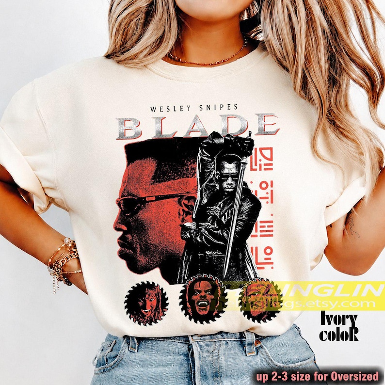 May include: An off-white t-shirt featuring a graphic print of Wesley Snipes as Blade. The design includes the text BLADE, a profile view of the character wearing sunglasses, a full-body illustration holding a sword, and three circular portraits.