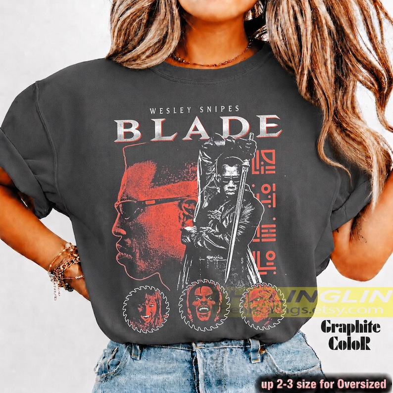 May include: A charcoal grey t-shirt featuring a red and white graphic print of Wesley Snipes as Blade holding a sword. The design includes the text WESLEY SNIPES BLADE, three circular saw blade icons with faces, and geometric patterns.