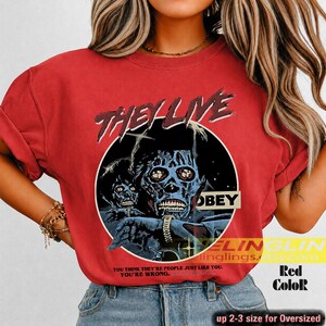 K&ouml;nnte beinhalten: Ein rotes T-Shirt mit einem Grafikdruck aus dem Film They Live. Das Design zeigt einen schwarzen kreisf&ouml;rmigen Rahmen mit zwei blau get&ouml;nten Alien-Figuren, dem Text "THEY LIVE" oben, "OBEY" auf einem Balken und dem Zitat "YOU THINK THEY'RE PEOPLE JUST LIKE YOU. YOU'RE WRONG."