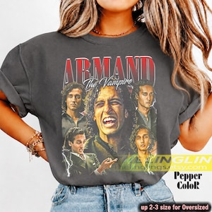 May include: A charcoal gray short-sleeve t-shirt featuring a graphic print of the character Armand from The Vampire. The design includes the text ARMAND The Vampire in red and white lettering, along with multiple portraits of the character.