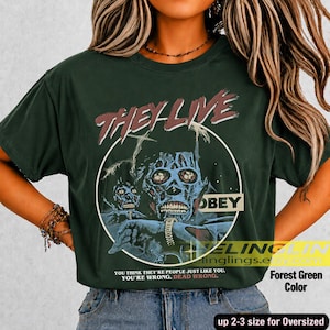 K&ouml;nnte beinhalten: Ein waldgr&uuml;nes T-Shirt mit einer Grafik einer totenkopfartigen Figur und dem Text THEY LIVE und OBEY. Unter der Grafik steht der Text: YOU THINK THEY ARE PEOPLE JUST LIKE YOU. YOU ARE WRONG. DEAD WRONG. Das T-Shirt hat kurze &Auml;rmel und einen Rundhalsausschnitt.