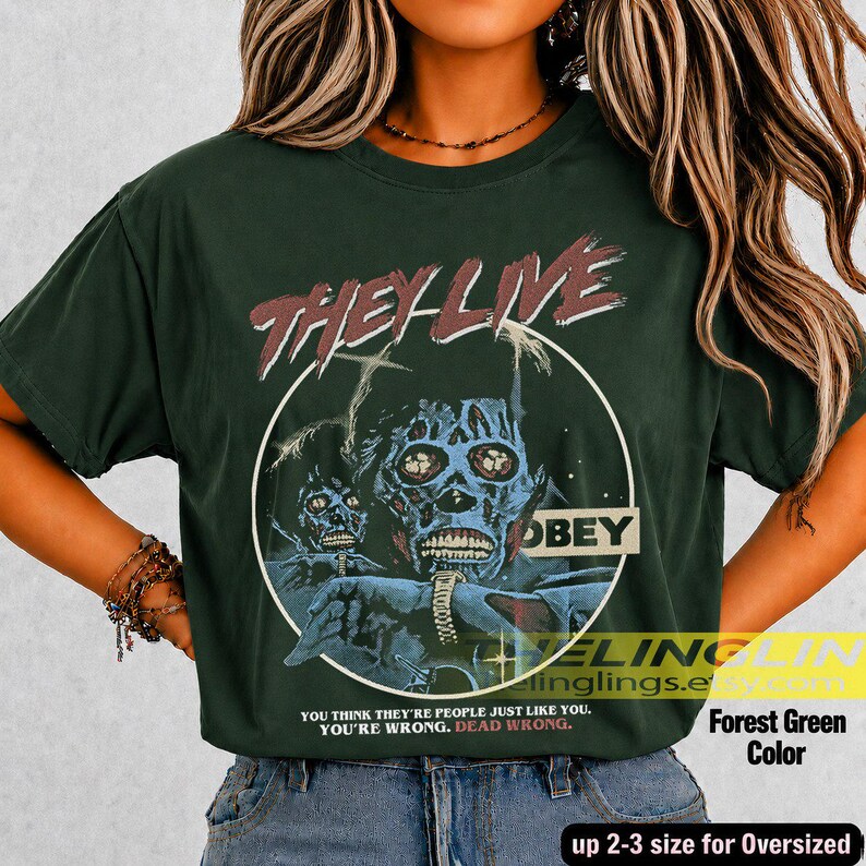 K&ouml;nnte beinhalten: Ein waldgr&uuml;nes T-Shirt mit einer Grafik einer totenkopfartigen Figur und dem Text THEY LIVE und OBEY. Unter der Grafik steht der Text: YOU THINK THEY ARE PEOPLE JUST LIKE YOU. YOU ARE WRONG. DEAD WRONG. Das T-Shirt hat kurze &Auml;rmel und einen Rundhalsausschnitt.