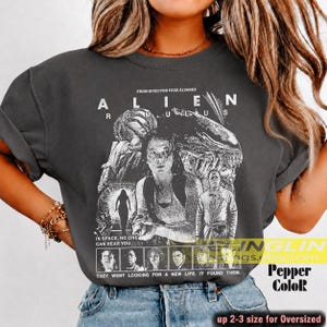 May include: Dark gray t-shirt featuring a black and white graphic from the movie "Alien: Romulus." The design includes the film's title, director's name, and the tagline "In space, no one can hear you." The shirt also has the text "They went looking for a new life. It found them."