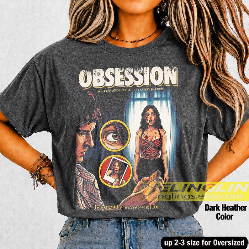 K&ouml;nnte beinhalten: Dunkelgraues meliertes T-Shirt mit dem Wort "OBSESSION" im Vintage-Stil. Das Shirt zeigt ein Filmplakat-Design mit Illustrationen eines Mannes, einer Frau und einem Polaroid-Foto. Der Text "Be careful who you wish for..." ist ebenfalls sichtbar.