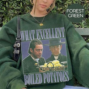 Puede incluir: Sudadera verde bosque con el texto "WHAT EXCELLENT BOILED POTATOES" y un gráfico vintage de dos hombres. La sudadera es de color liso, con cuello redondo y mangas largas.