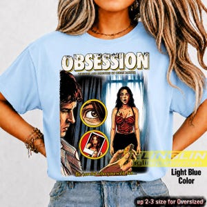 K&ouml;nnte beinhalten: Hellblaues T-Shirt mit einem Filmplakat-Design f&uuml;r "Obsession". Die Grafik zeigt Illustrationen eines Mannes, einer Frau und den Text "Be careful who you wish for...". Erh&auml;ltlich in bis zu 2-3 Gr&ouml;&szlig;en f&uuml;r &uuml;bergro&szlig;e Passformen.
