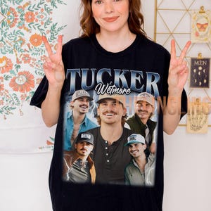 Puede incluir: Camiseta negra con un gráfico de Tucker Wetmore, con múltiples imágenes de él. El texto "TUCKER Wetmore" se muestra en un diseño azul y blanco. La persona de la imagen lleva la camiseta y hace el signo de la paz.