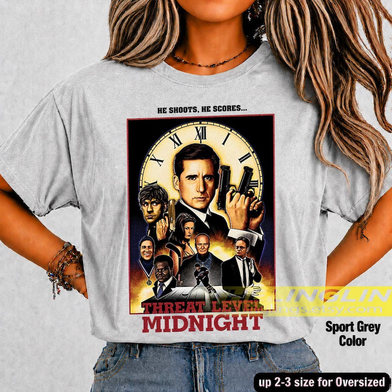 May include: A light gray t-shirt featuring a graphic print of a clock face background with multiple character portraits and the text "HE SHOOTS, HE SCORES..." at the top and "MIDNIGHT" at the bottom, arranged in a movie poster style layout.