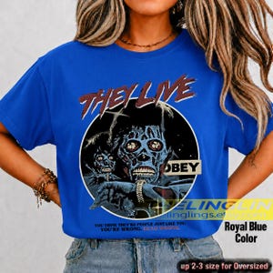 K&ouml;nnte beinhalten: Ein k&ouml;nigsblaues Kurzarm-T-Shirt mit einem Grafikdruck einer skelettierten Figur und dem Text THEY LIVE und OBEY. Unter der Grafik steht der Text: YOU THINK YOU ARE PEOPLE JUST LIKE YOU. YOU ARE WRONG. DEAD WRONG. Das Shirt hat einen Rundhalsausschnitt.