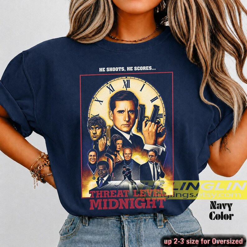 May include: A navy blue t-shirt featuring a graphic print of the movie poster for Threat Level Midnight. The design includes a large clock face, multiple character portraits, and the text HE SHOOTS, HE SCORES... and THREAT LEVEL MIDNIGHT.