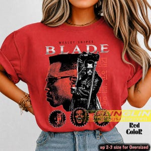 May include: A red t-shirt featuring a graphic print of Wesley Snipes as Blade. The design includes the text "WESLEY SNIPES BLADE" above a large portrait and a full-body figure holding a sword, with three smaller circular character portraits below.