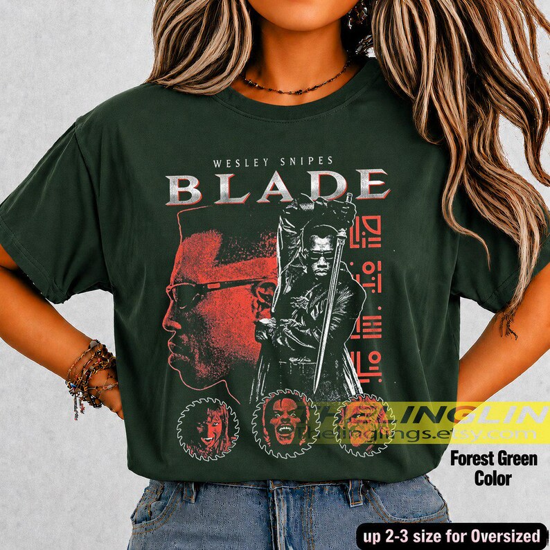 May include: A forest green short-sleeve t-shirt featuring a graphic print of Wesley Snipes as Blade. The design includes the text BLADE, a large profile silhouette, a central figure holding a sword, and three circular character portraits.