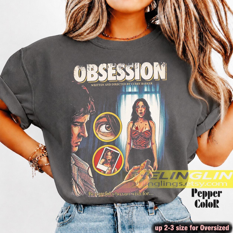 K&ouml;nnte beinhalten: Dunkelgraues T-Shirt mit einem Vintage-Filmplakat-Design f&uuml;r "Obsession". Die Grafik zeigt Illustrationen eines Mannes, einer Frau und eines Auges. Der Text enth&auml;lt "OBSESSION" und "WRITTEN AND DIRECTED BY CURRY BAKKER."