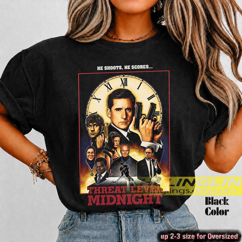 May include: A black t-shirt featuring a graphic print of a movie poster titled Threat Level Midnight. The design includes a large clock face, multiple character portraits, and the text HE SHOOTS, HE SCORES... above the central figure holding a gun.
