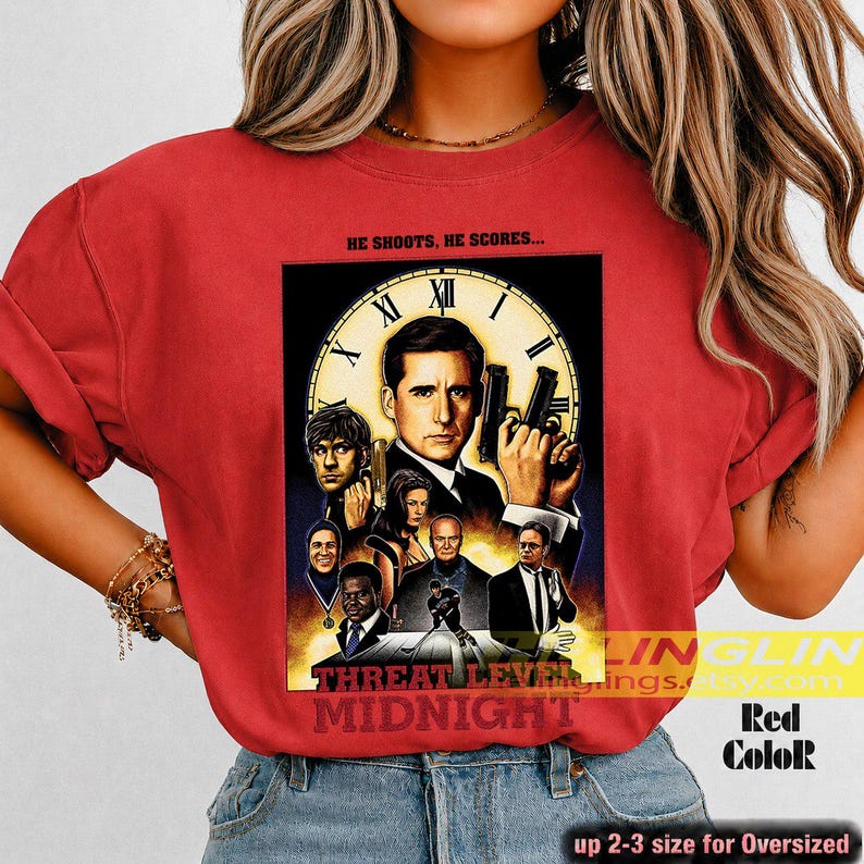 May include: A red t-shirt featuring a graphic print of the movie poster for Threat Level Midnight. The design includes a large clock face background, a central male figure holding a gun, and several smaller character portraits below.