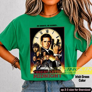 May include: An Irish green t-shirt featuring a graphic print of the movie poster for Threat Level Midnight. The design includes a large clock face, multiple character portraits, and the text HE SHOOTS, HE SCORES and THREAT LEVEL MIDNIGHT.
