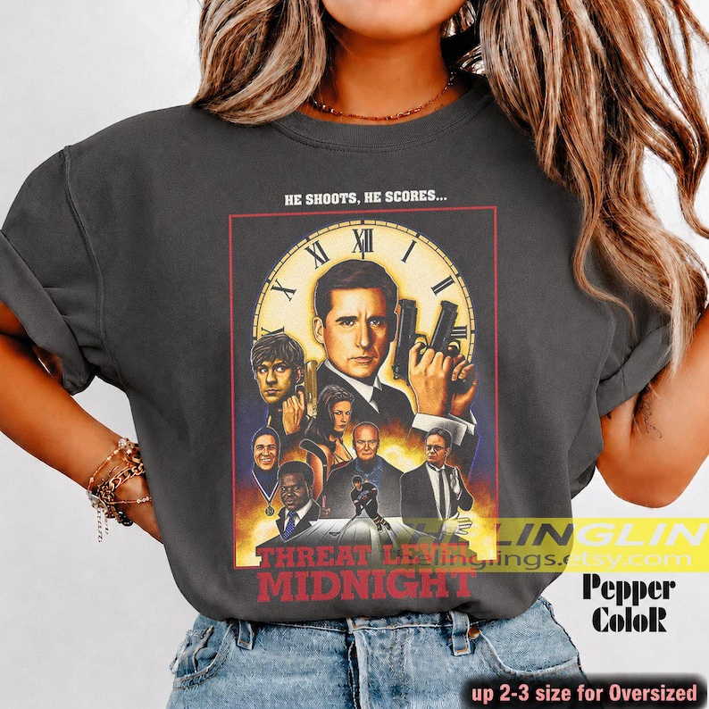 May include: A charcoal gray crewneck t-shirt featuring a graphic print of the movie poster for Threat Level Midnight. The design includes a large clock face, multiple character portraits, and the text HE SHOOTS, HE SCORES... and THREAT LEVEL MIDNIGHT.