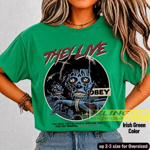 K&ouml;nnte beinhalten: Ein hellgr&uuml;nes Kurzarm-T-Shirt mit einem Grafikdruck einer skelettierten Figur und dem Text THEY LIVE und OBEY. Unter der Grafik steht der Text: YOU THINK THEY'RE PEOPLE JUST LIKE YOU. YOU'RE WRONG.