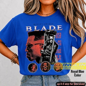May include: A royal blue t-shirt featuring a graphic print of Wesley Snipes as Blade. The design includes a large profile portrait, a figure holding a sword, and three circular character icons. The text reads WESLEY SNIPES BLADE.
