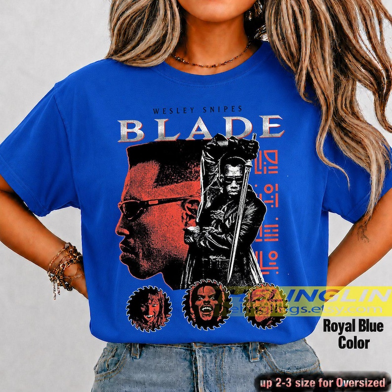 May include: A royal blue t-shirt featuring a graphic print of Wesley Snipes as Blade. The design includes a large profile portrait, a figure holding a sword, and three circular character icons. The text reads WESLEY SNIPES BLADE.