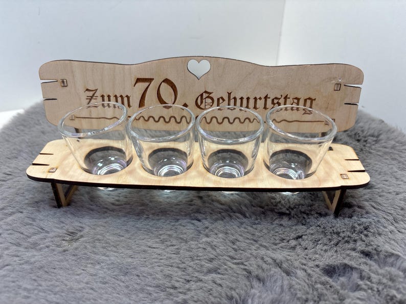 May include: Wooden shot glass holder with the text "Zum 70. Geburtstag" and a heart. The holder has four shot glasses.