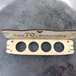 May include: Wooden box with five round cutouts and a sign that reads "Zum 70. Geburtstag".