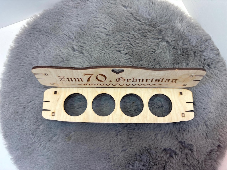 May include: Wooden box with five round cutouts and a sign that reads "Zum 70. Geburtstag".