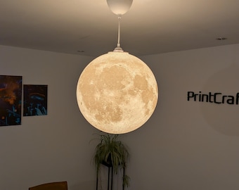 May include: A spherical pendant light fixture featuring a detailed, textured surface that mimics the appearance of the moon. The lamp is suspended from the ceiling by a white cord and a white canopy, emitting a warm, soft glow from within.