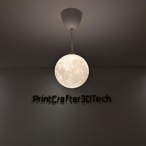 Eine kugelförmige Pendelleuchte mit einer detaillierten, strukturierten Oberfläche, die dem Mond ähnelt und an einer weißen Deckenhalterung hängt. Unter der beleuchteten Mondlampe ist der Text PrintCrafter3DTech in dunkler, fetter Schrift zu sehen.