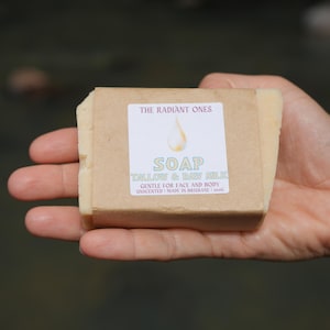Puede incluir: Una pastilla de jabón envuelta en papel marrón con una etiqueta que dice "THE RADIANT ONES SOAP TALLOW & RAW MILK GENTLE FOR FACE AND BODY UNSCENTED MADE IN BRISBANE 100g"