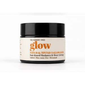 May include: A black cylindrical jar of The Radiant Ones Glow natural tinted tallow balm. The cream-colored label features orange text reading glow, with additional text: Natural Tinted Tallow Balm, Sun-kissed Radiance & Sheer Coverage, Tallow, Non-nano Zinc, Botanicals.